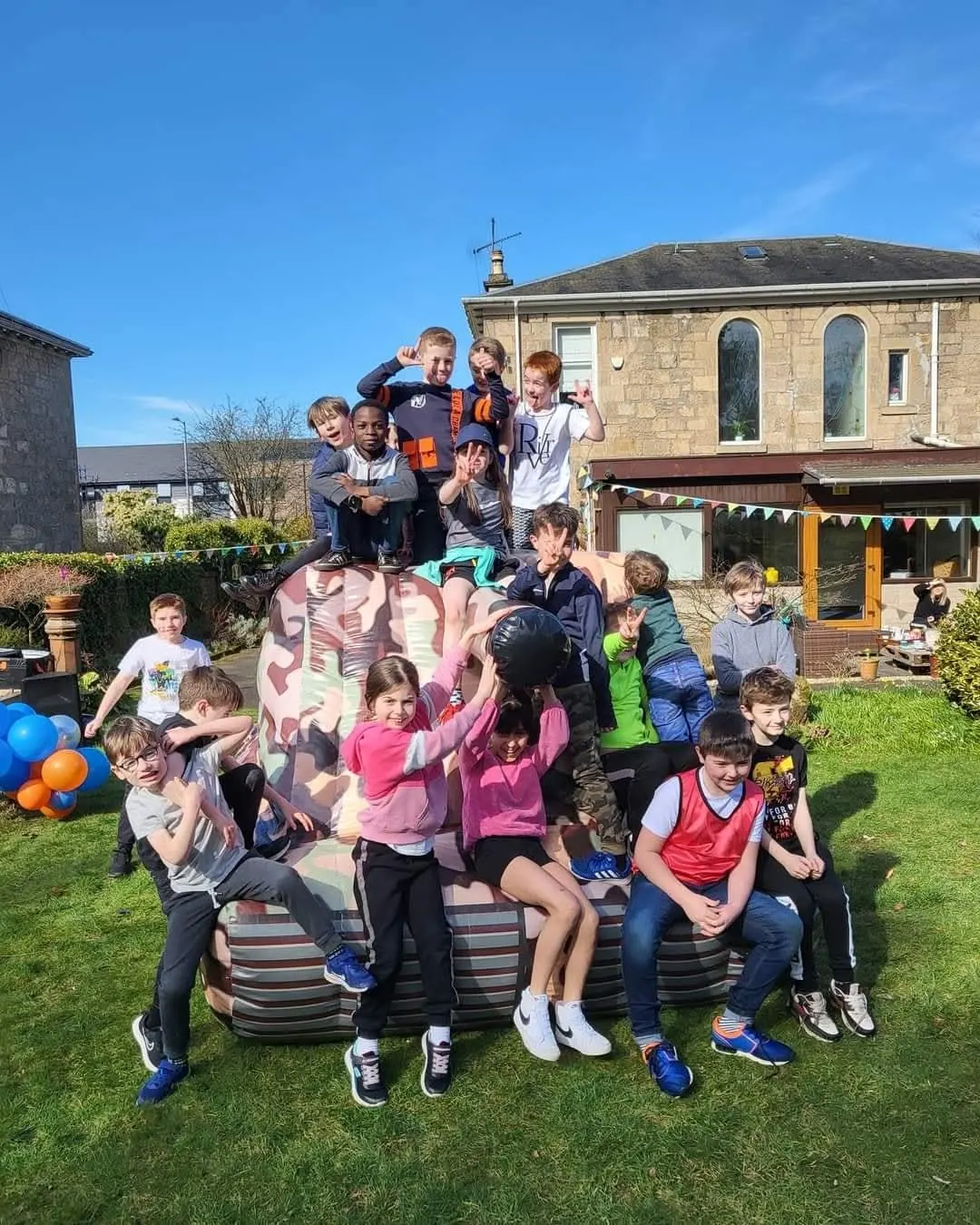 A birthday group climbing on the inflatable tank in a sunny back garden after their battle