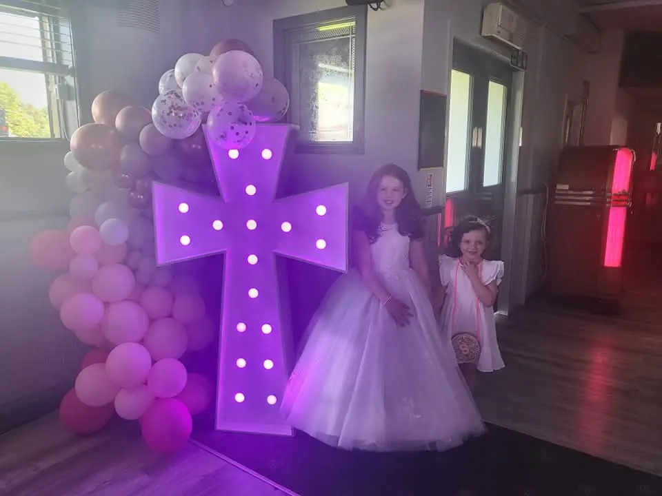 Two girls in white dresses beside a balloon display at a family celebration in Glasgow