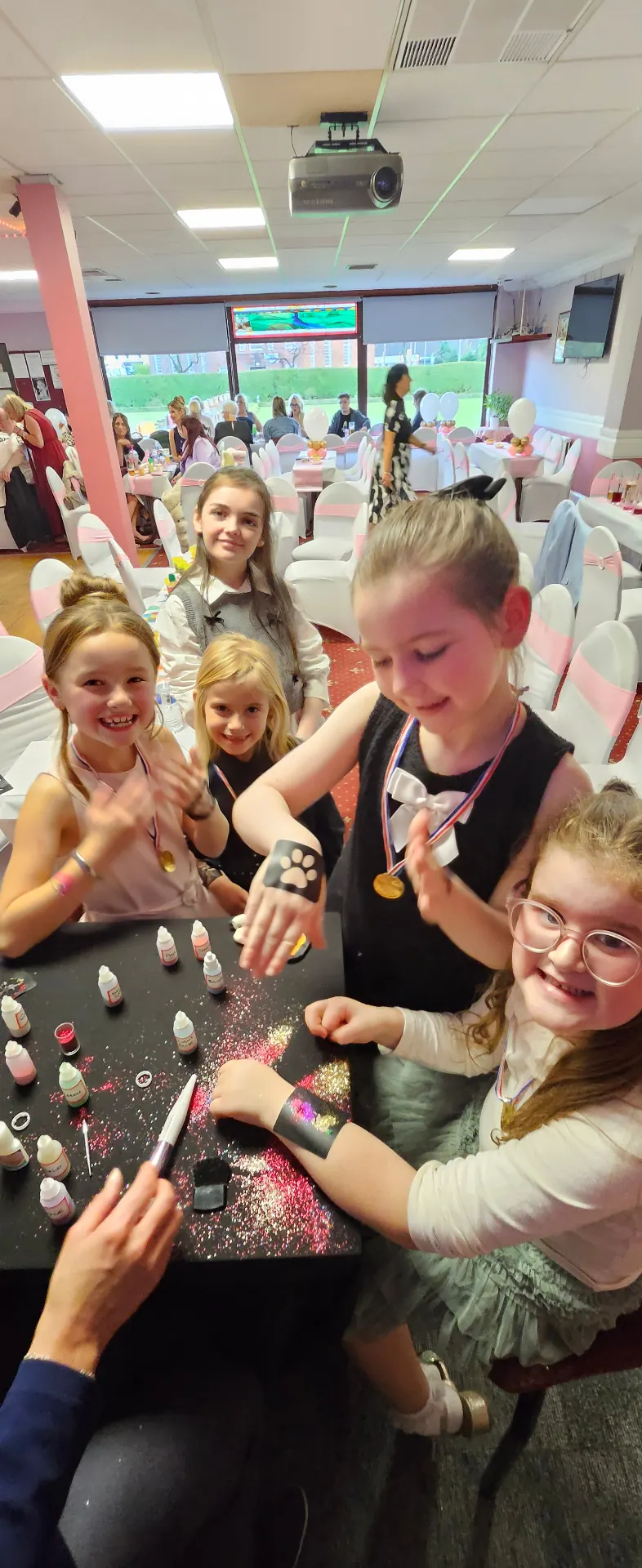 Girls smiling as they get glitter tattoos at a family celebration party table