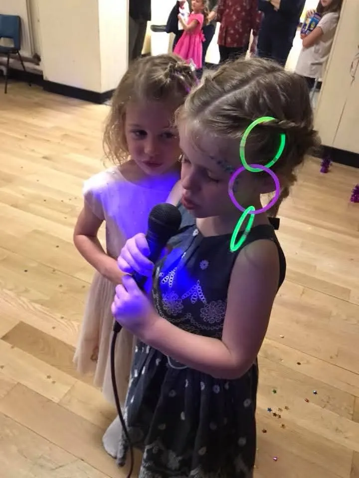 Two girls sharing a microphone and singing along during a hosted party game