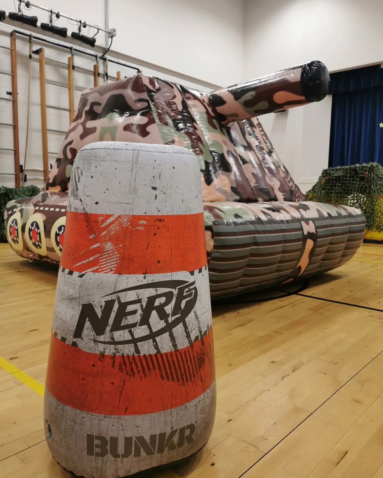 Giant inflatable tank and a Nerf bunker barricade set up in a school gym hall