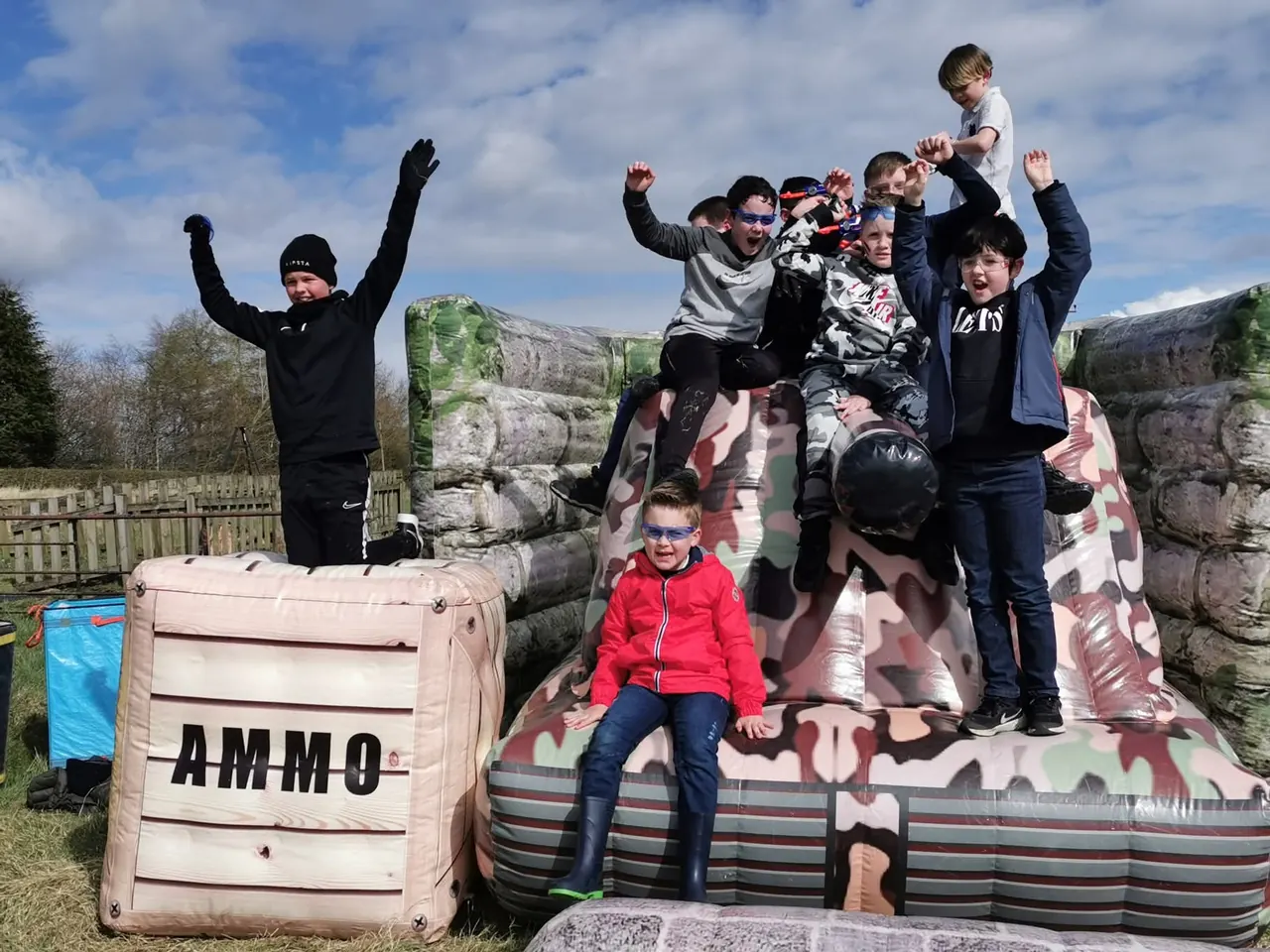 Children celebrating on top of inflatable cover and an ammo crate at an outdoor Nerf battlefield