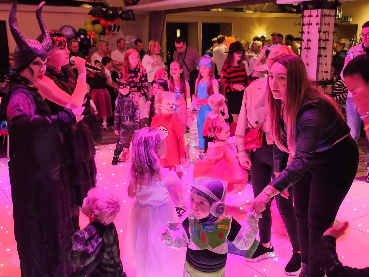 A costumed party host with a microphone leading a game as children join in under pink lighting