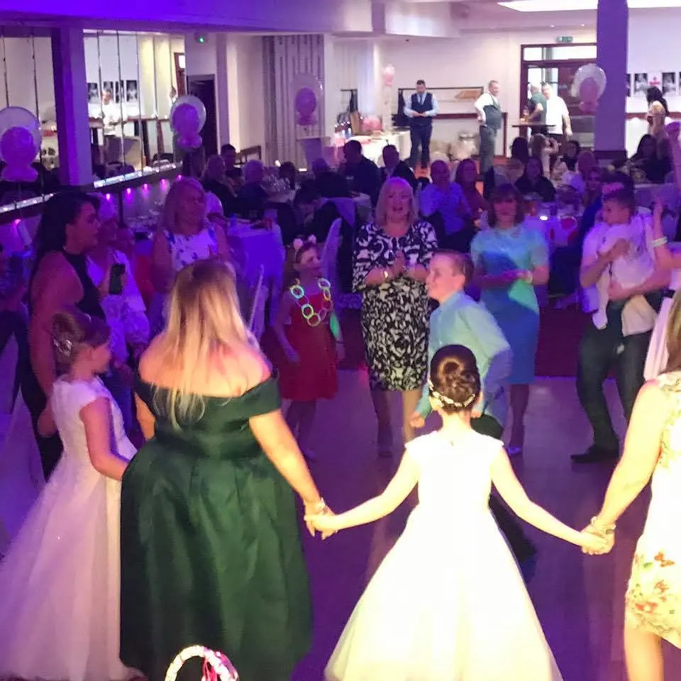 Children and families enjoying a Communion, Christening or Naming Day party in Glasgow, holding hands in a dance circle
