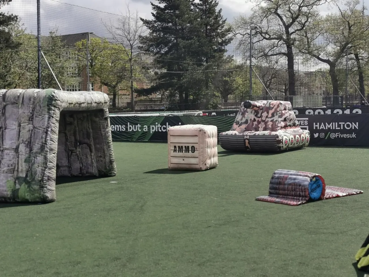 Inflatable barricades, an ammo crate and a camouflage tank laid out on an outdoor all-weather pitch