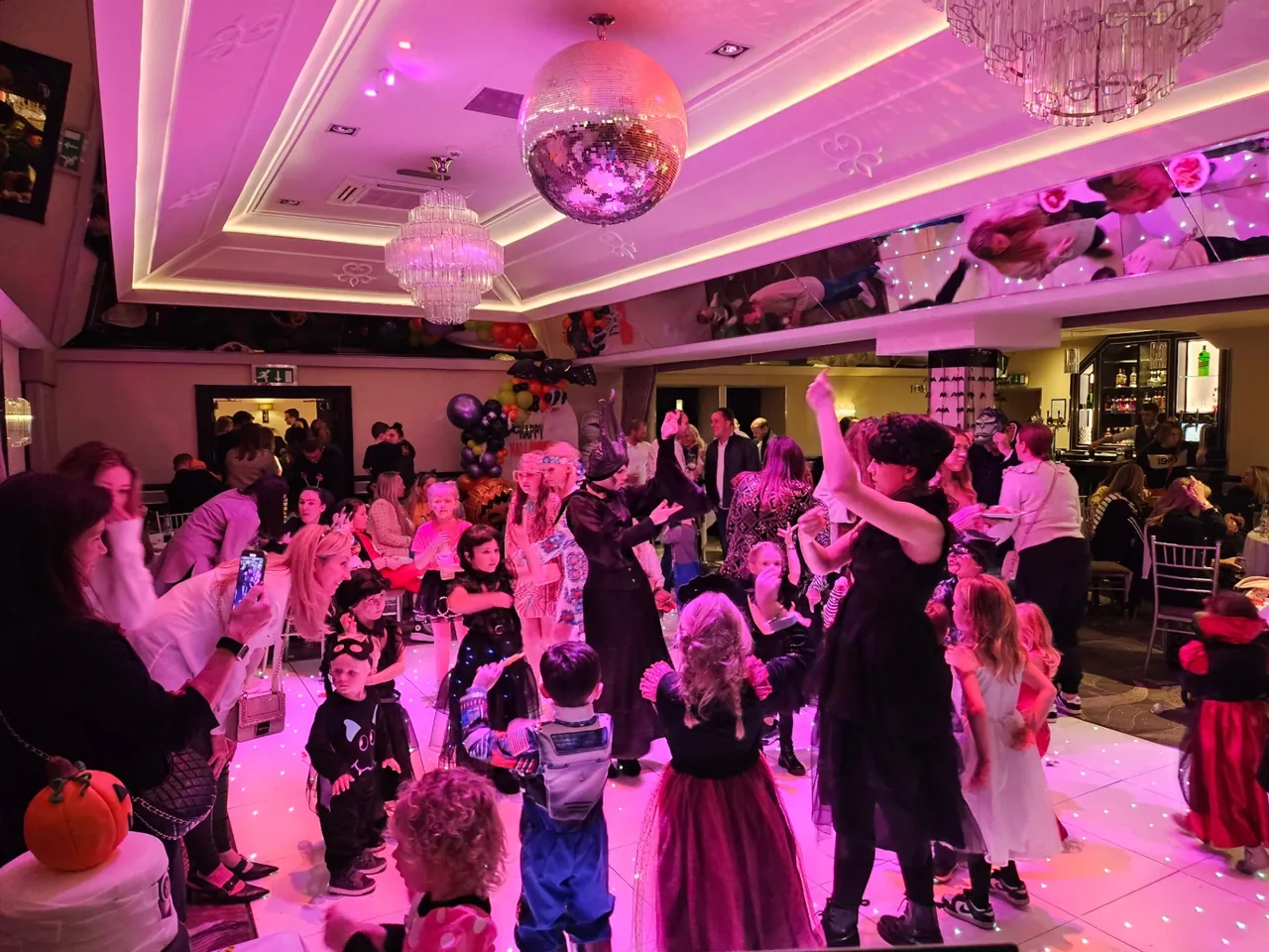 Children in Halloween costumes dancing at a themed disco with balloons and a mirrorball