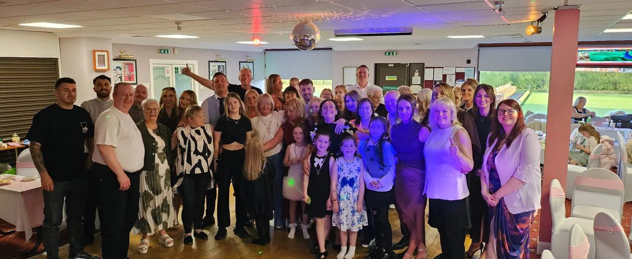 Adults and children gathered for a group photo on the dance floor beneath a mirrorball