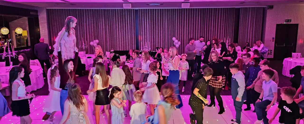 Children dancing on a white LED dance floor under purple lighting at a family celebration